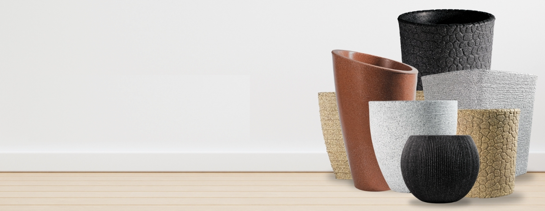A group of six modern cylindrical and tapered planters in various materials and colors, including textured black, matte brown, woven beige, and smooth gray, arranged on a light wood floor against a white wall.